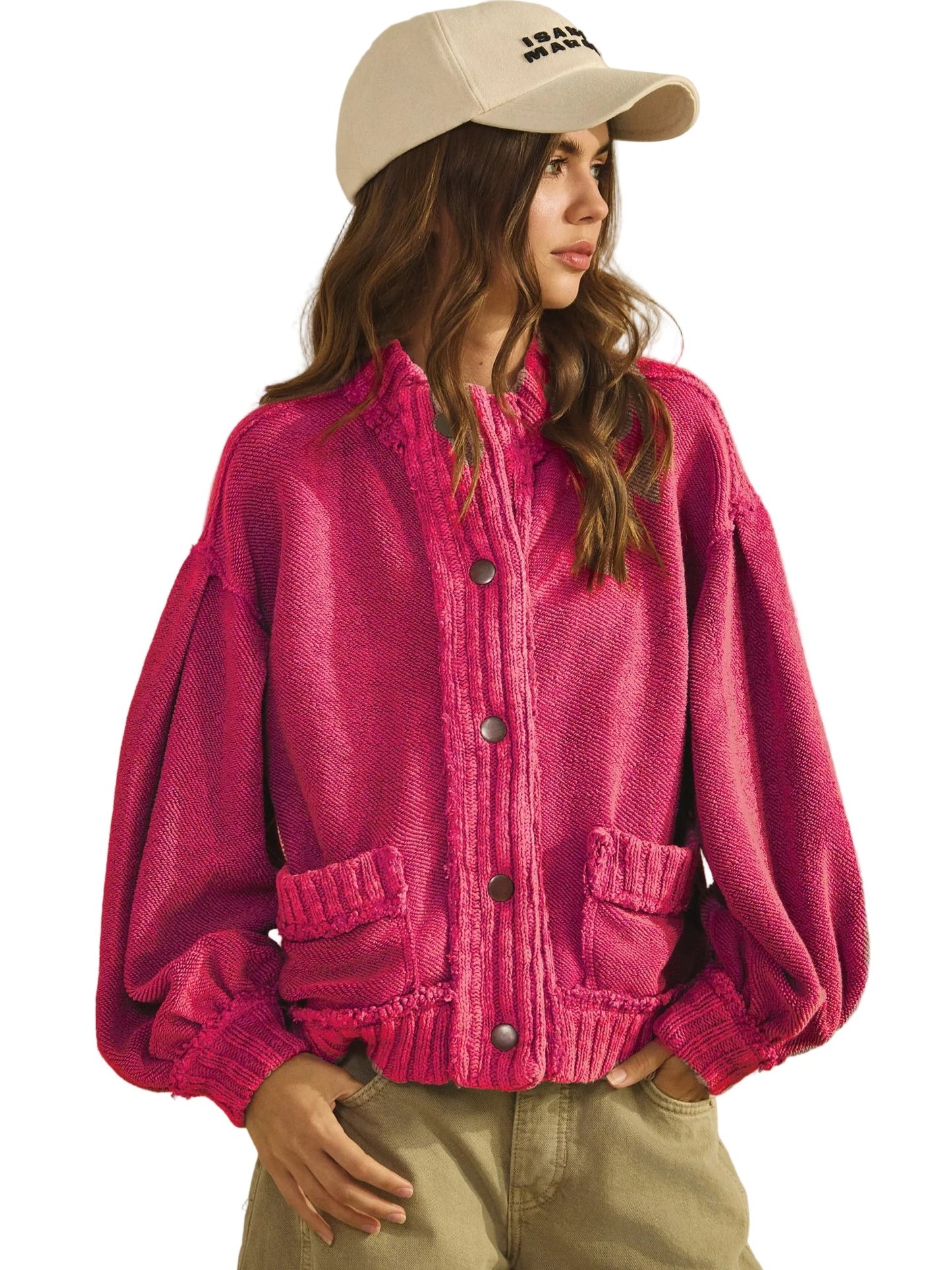 Person wearing a pink knitted cardigan and beige cap on a plain background