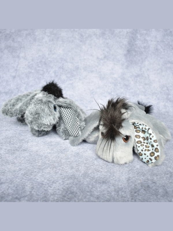 A plush stuffed animal toy shaped like a gray elephant lying on a soft light gray fabric background. The toy has dark brown faux fur on its head and ears, a black-and-white checkered necktie, and a light blue patterned inner ear.