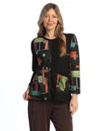 A woman modeling a black long-sleeve jacket with colorful geometric patchwork panels in green, orange, and red, paired with brown pants against a white background.