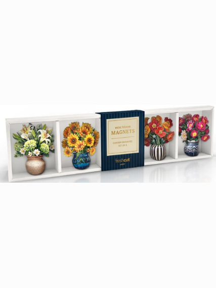 A decorative floral magnet set displayed on a white shelf. The set includes four square magnets in vases with green, yellow, orange, and pink flowers, alongside a dark blue book-style cover labeled 'MAGNETS'.
