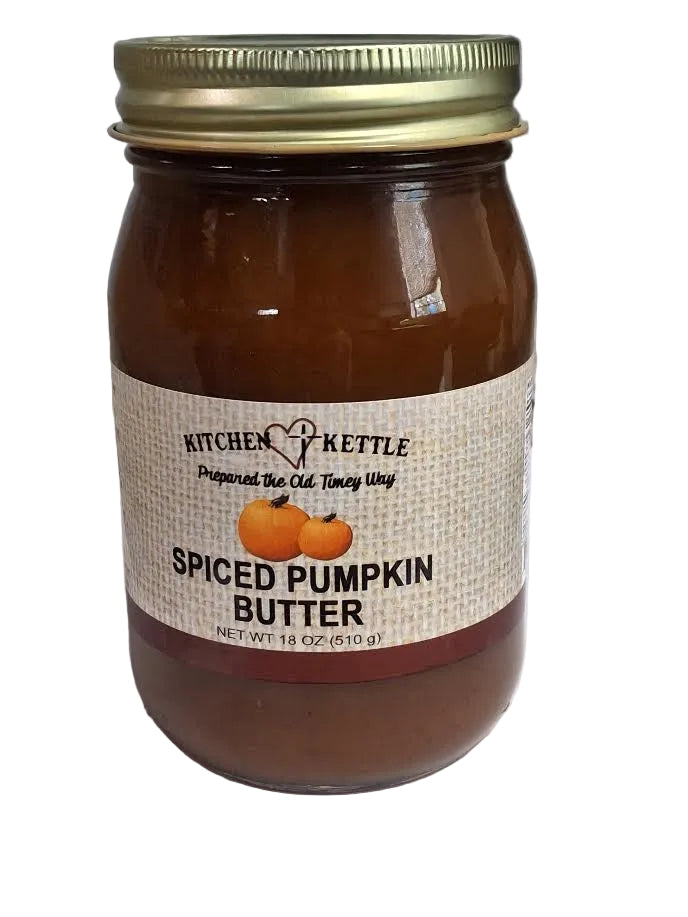 A glass jar of Kitchen Kettle Spiced Pumpkin Butter with a gold metal lid and a beige label featuring two small pumpkins, set on a white surface with a gray background.