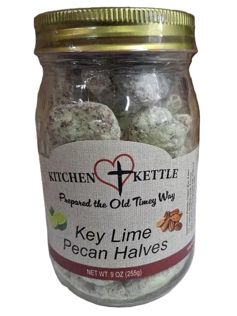 A glass jar of Kitchen Kettle Key Lime Pecan Halves filled with green pecan halves, set against a background of cardboard boxes.