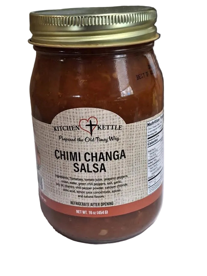 A glass jar of Kitchen Kettle Chimi Changa Salsa with a gold metal lid and a beige label, set on a white surface with a kitchen countertop in the background.