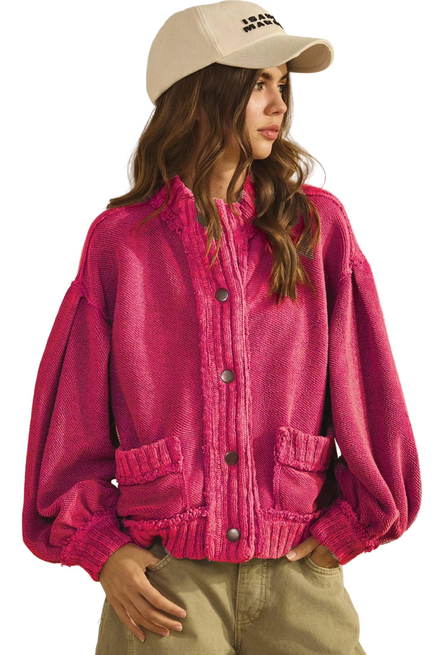 Person wearing a pink knitted cardigan and beige cap on a plain background