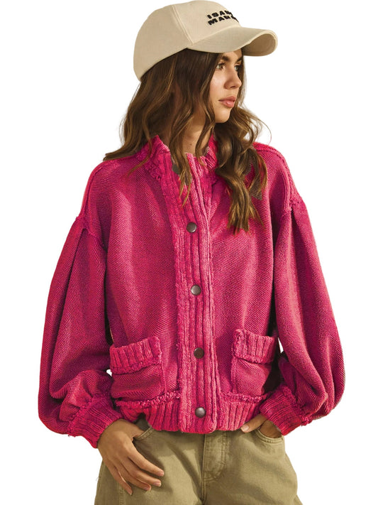 Person wearing a pink knitted cardigan and beige cap on a plain background