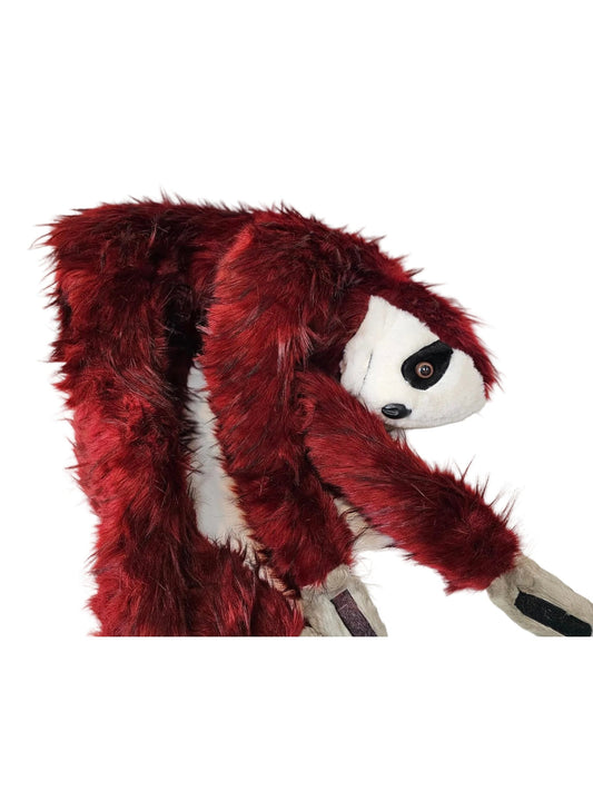 A plush sloth toy wearing a dark red faux-fur costume, hanging upside down against a white wall.