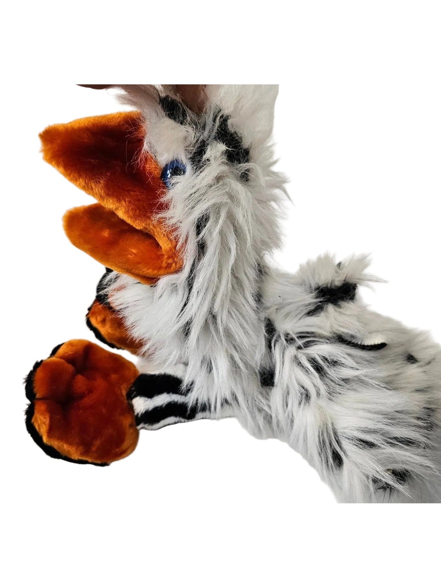 A close-up of a fluffy animal-style plush or costume body with white fur, black patches, bright orange inner ears, and orange paw pads, being held by a human hand against a white indoor background.