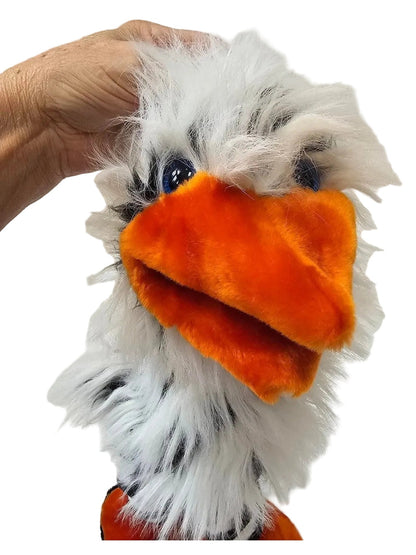 A fluffy bird plush toy with white and black feathers, a bright orange beak, and orange feet, being held by a hand against a white paneled wall.