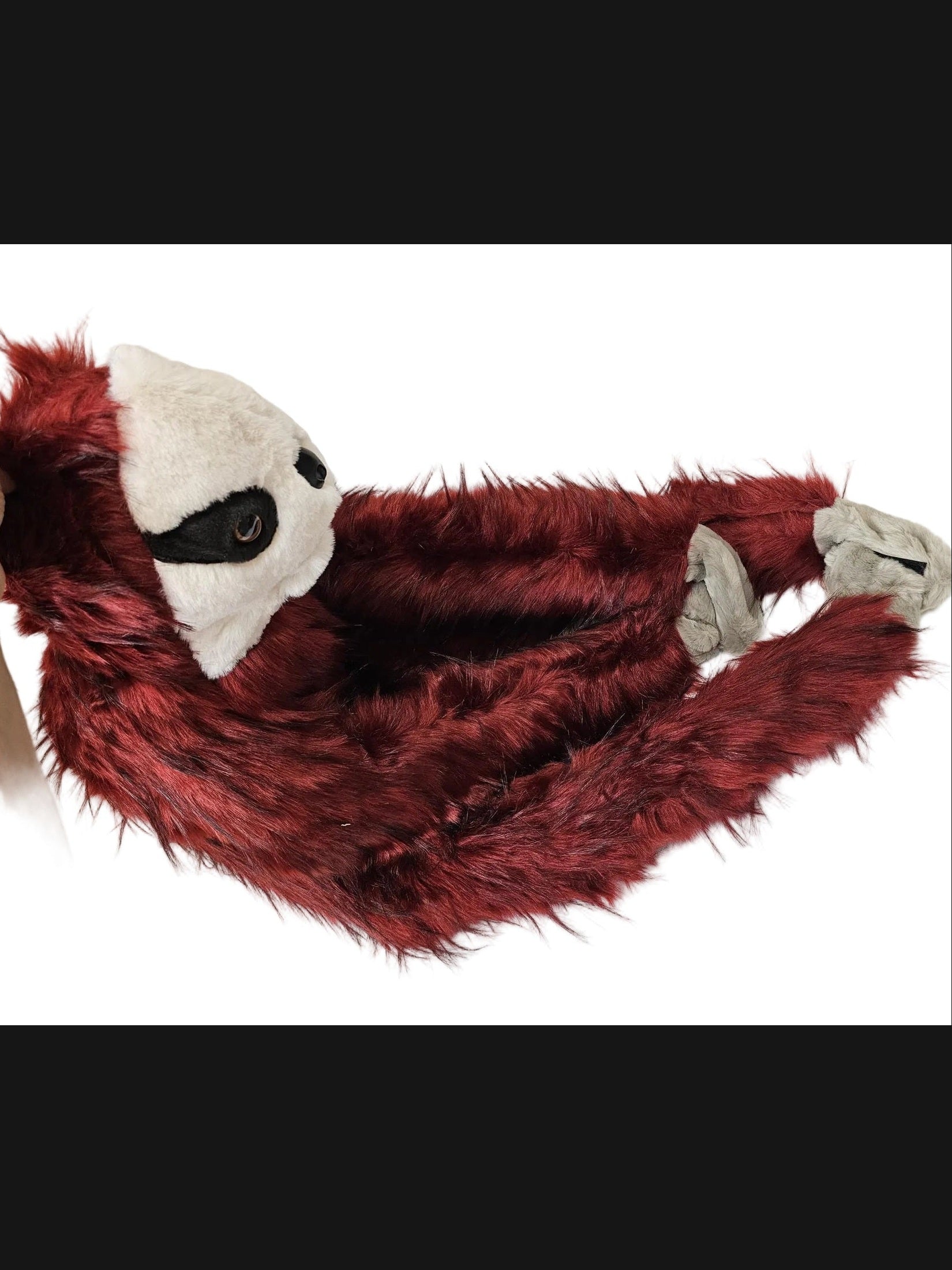 A red faux fur costume or hood with a white face panel, black eye details, and gray claw-like hand details, being held by a person's hand on a white surface.
