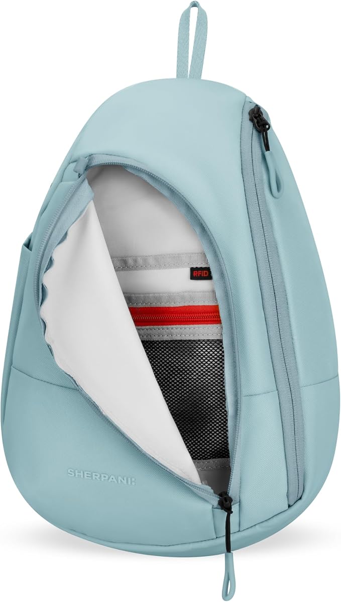 A light blue backpack shown open to display its interior, including a white inner lining, a gray mesh pocket, and a red accent strip inside. The brand name 'SHERBANI' is subtly printed near the bottom left corner.