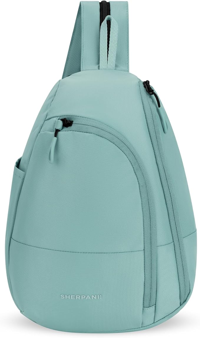 A light mint green sling backpack by Sherpani, featuring a single shoulder strap, a front zippered pocket, and a curved lower body, shown against a plain white background.