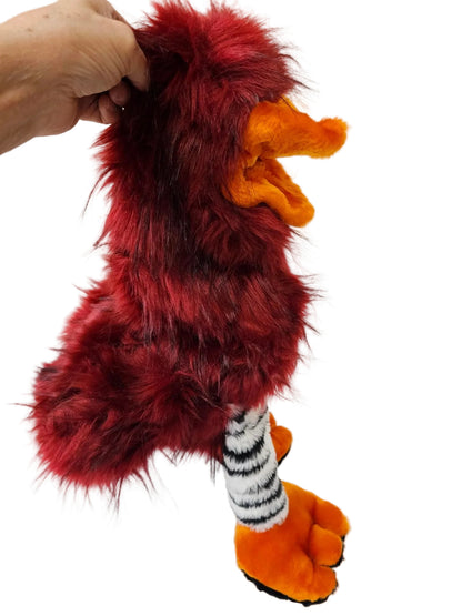 A red furry costume accessory with orange feet and a black-and-white striped leg, held by a hand against a white paneled background.