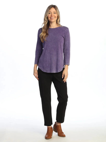 Woman wearing a purple long-sleeve top and black pants on a white background