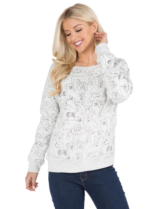 A blonde woman wearing a white long-sleeve crewneck sweatshirt with a black line art pattern of cartoon dogs, paired with dark blue jeans, against a light gray studio background.