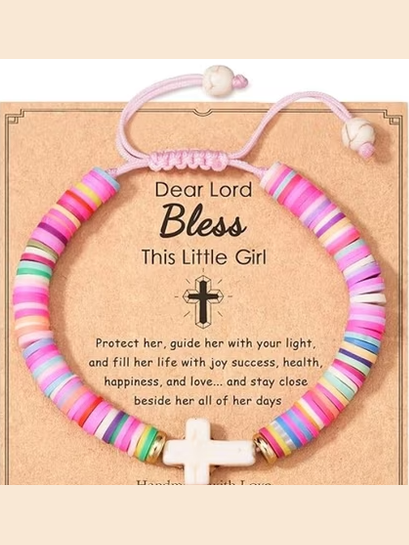 A colorful beaded cord bracelet with a white cross charm, presented on a tan gift card with printed blessing text. The bracelet features multiple pastel and bright stripes in pink, blue, green, yellow, and white, with a small gold-toned bead accent near the cross.