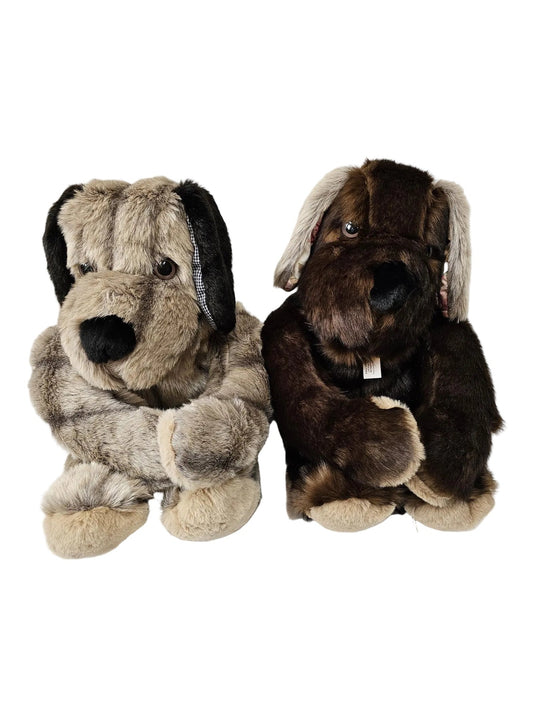 Two plush stuffed dogs sitting side by side on a white surface against a white paneled wall. The dog on the left is light gray and beige with black ears and nose.