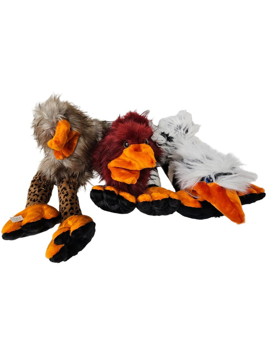 Three plush toy birds arranged side by side on a white surface against a white paneled wall. The left toy resembles a brown and black spotted bird with gray-brown feathers and an orange beak.