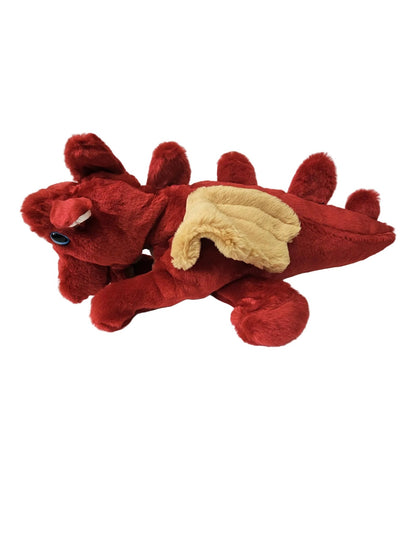 A red plush dragon toy with beige wings, lying on a white surface against a white paneled wall.