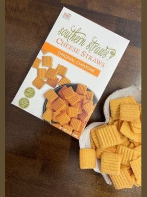 Box of southern strands cheese straws on a wooden surface with cheese straws beside it.